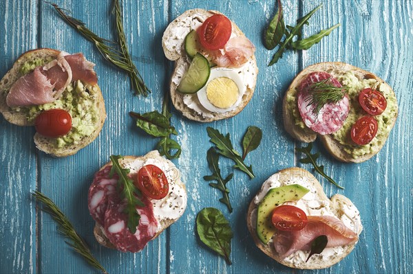 Sandwiches with curd cheese and vegetables and sausage on wooden background