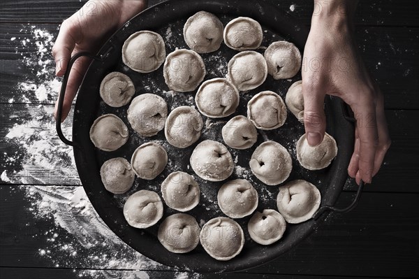 Handmade homemade dumplings on a decorative metal tray on a wooden background with flour. Diy meat dumplings