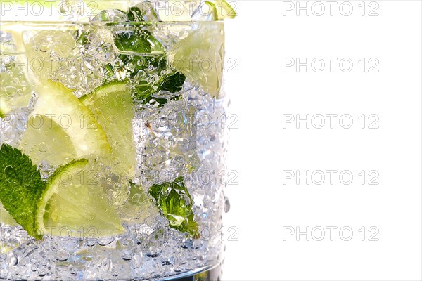 Glass of Mojito summer alcoholic cocktail with ice cubes mint and lime on white background with raw lime and mint leaf