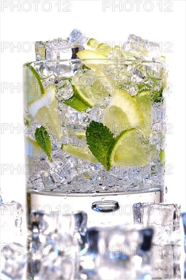 Glass of Mojito summer alcoholic cocktail with ice cubes mint and lime on white background with raw lime and mint leaf