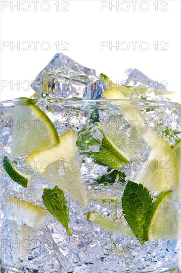 Glass of Mojito summer alcoholic cocktail with ice cubes mint and lime on white background with raw lime and mint leaf