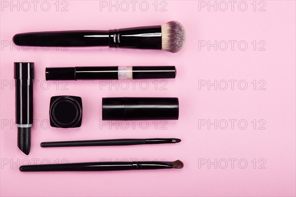 Set of brushes and cosmetic products on a pink background