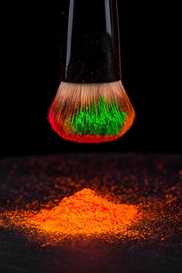 Cheek brush with neon cosmetic powder colorful pile and isolated on black background