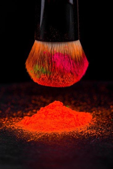 Cheek brush with neon cosmetic powder colorful pile and isolated on black background