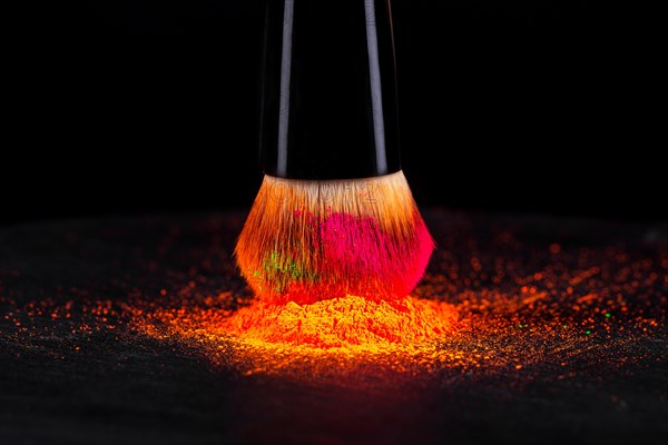 Cheek brush with neon cosmetic powder colorful pile and isolated on black background