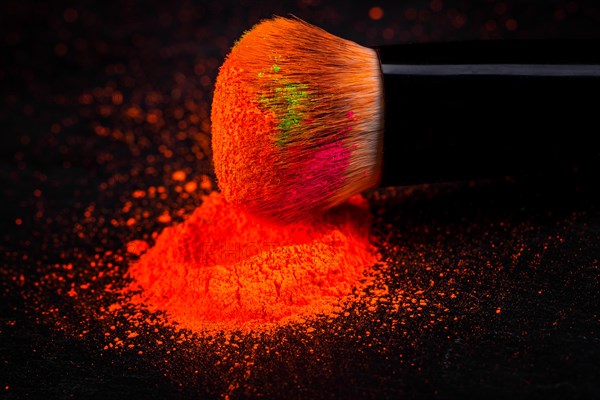 Cheek brush with neon cosmetic powder colorful pile and isolated on black background