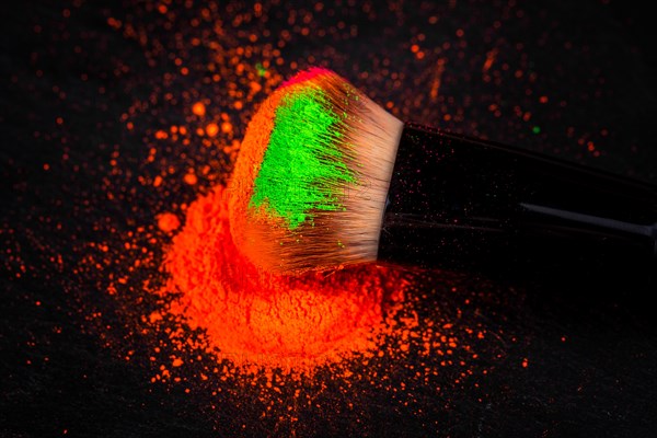 Cheek brush with neon cosmetic powder colorful pile and isolated on black background