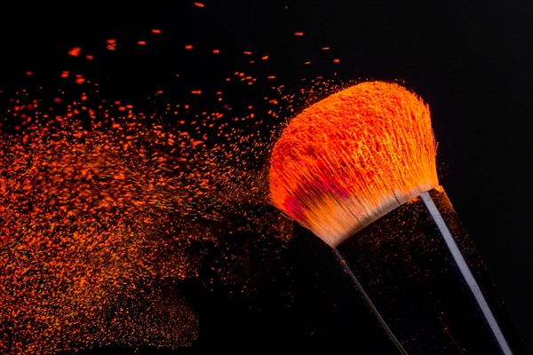 Cheek brush with neon cosmetic powder colorful spray and isolated on black background