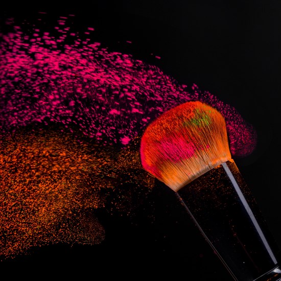 Cheek brush with neon cosmetic powder colorful spray and isolated on black background