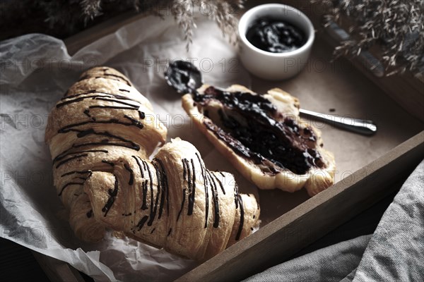 Croissants with chocolate and jam on a wooden breakfast tray