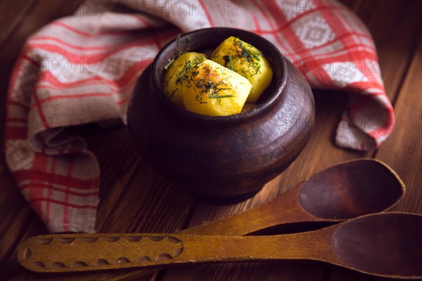 Baked potato in old pot on wooden background with pickled cabbage and cucumber