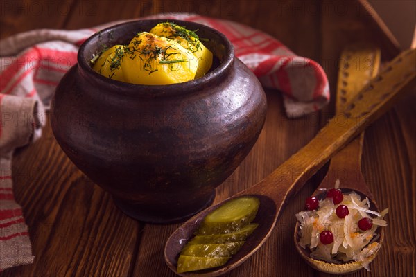 Baked potato in old pot on wooden background with pickled cabbage and cucumber