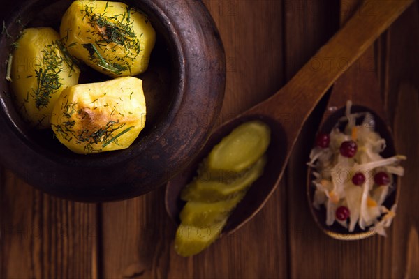 Baked potato in old pot on wooden background with pickled cabbage and cucumber