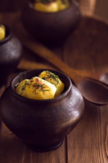 Baked potato in old pot on wooden background with pickled cabbage and cucumber