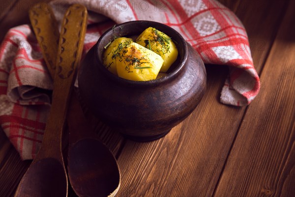 Baked potato in old pot on wooden background with pickled cabbage and cucumber