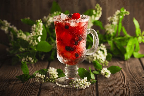 Berry soft drink with ice on a wooden background with flowers