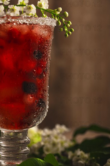 Berry soft drink with ice on a wooden background with flowers