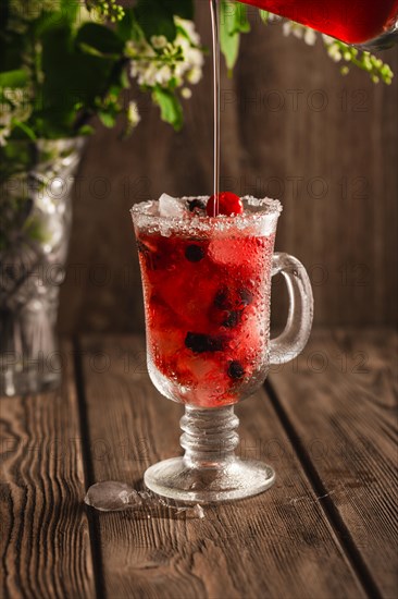 Berry soft drink with ice on a wooden background with flowers