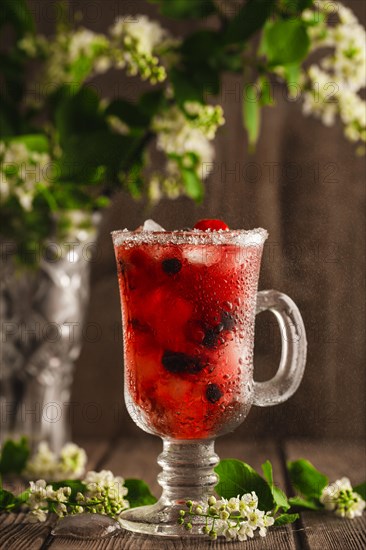 Berry soft drink with ice on a wooden background with flowers