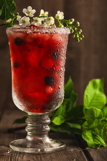 Berry soft drink with ice on a wooden background with flowers