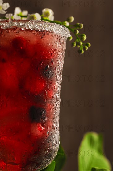 Berry soft drink with ice on a wooden background with flowers