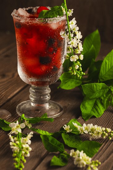 Berry soft drink with ice on a wooden background with flowers