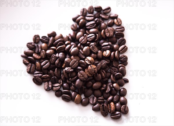 Grains of roasted coffee in the shape of heart on a white plate