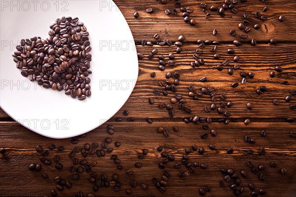 Grains of roasted coffee in the shape of heart on a white plate