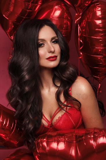 Sexy woman in red lace lingerie and balloons with hearts posing in the studio on Valentine's Day