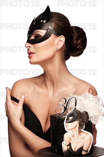 Beautiful woman pastry chef in cat mask and black dress with a cake in her hands