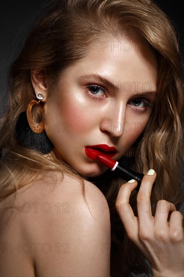 Beautiful girl with red lips and classic makeup and curls with lipstick in hand. Beauty face. Photo taken in the studio
