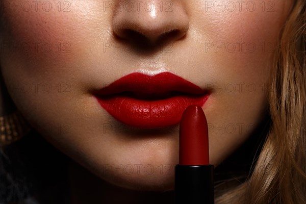 Beautiful girl with red lips and classic makeup and curls with lipstick in hand. Beauty face. Photo taken in the studio