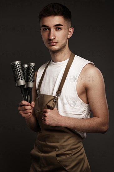 Handsome man hairdresser in a working uniform with brushing combs in his hands. Photo taken in the studio