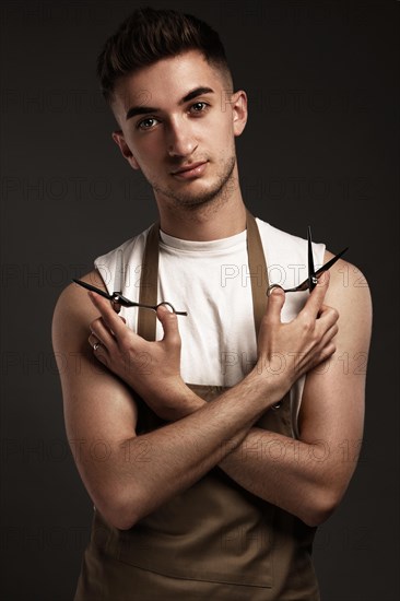 Handsome man hairdresser in a working uniform with scissors in his hands. Photo taken in the studio