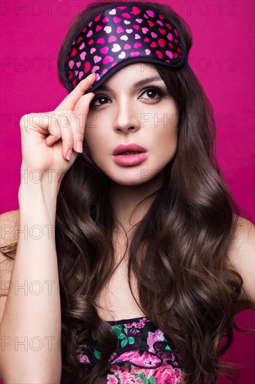 Funny young woman in sleeping mask and pajamas on a pink background. The beauty of the face. Photos shot in studio