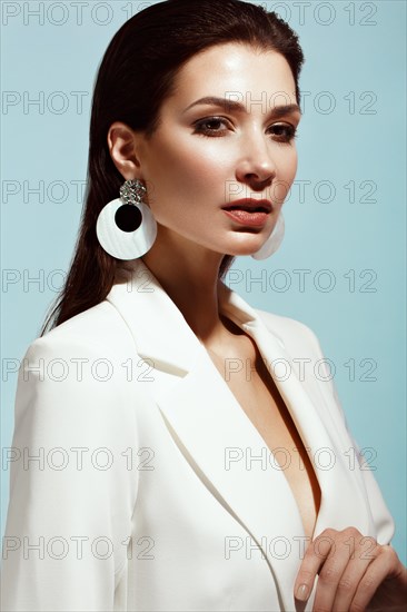 Beautiful girl with classic make-up and hair-style in a trendy designer white jacket posing in a studio. Beauty face