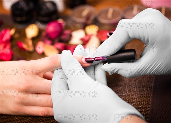 Closeup finger nail care by manicure specialist in beauty salon. Manicurist paints nails with red nail polish