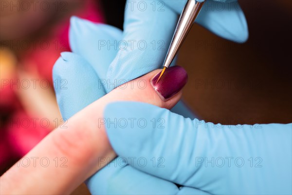 Closeup finger nail care by manicure specialist in beauty salon. Manicurist paints nails with red nail polish