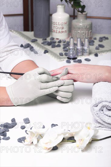 Closeup finger nail care by manicure specialist in beauty salon. Manicurist paints nails with nail polish