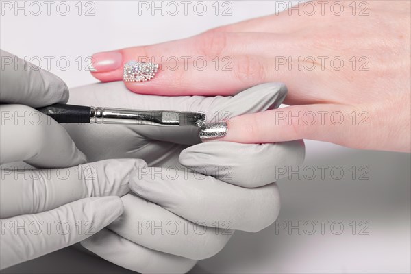 Closeup finger nail care by manicure specialist in beauty salon. Manicurist paints nails with nail polish