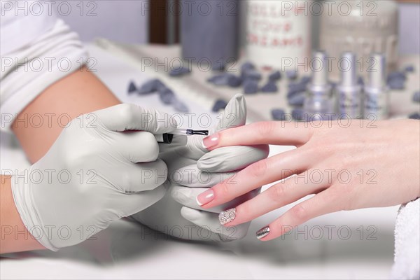 Closeup finger nail care by manicure specialist in beauty salon. Manicurist paints nails with nail polish