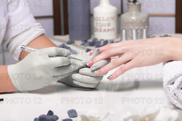 Closeup finger nail care by manicure specialist in beauty salon. Manicurist paints nails with nail polish