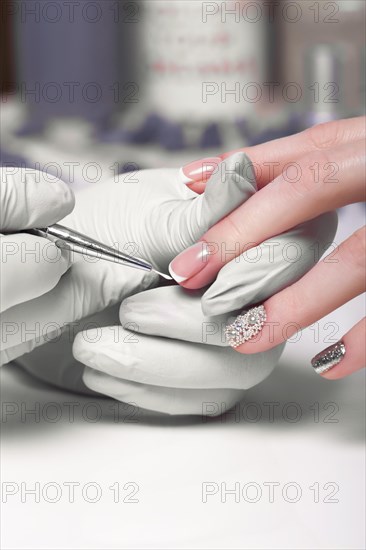 Closeup finger nail care by manicure specialist in beauty salon. Manicurist paints nails with nail polish