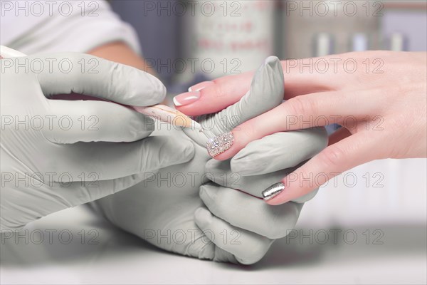 Closeup finger nail care by manicure specialist in beauty salon. Manicurist Glues rhinestones on nails