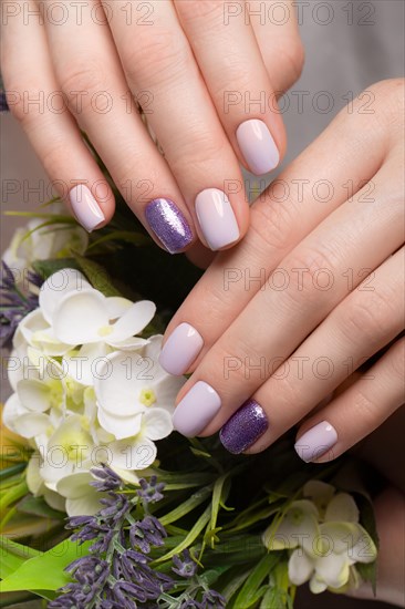 Purple neat manicure on female hands on a background of flowers. Nail design