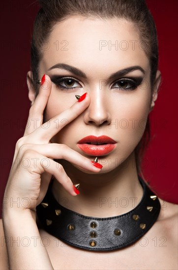 Beautiful woman in gothic style with evening makeup and red nails with thorns. Picture taken in a studio on a red background