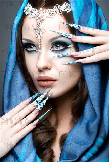 Beautiful girl in eastern Arabic image with long nails and bright blue make-up. Picture taken in the studio on a gray background