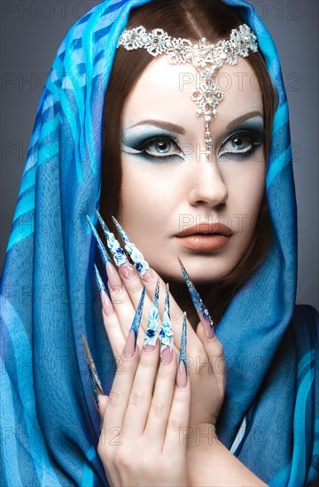 Beautiful girl in eastern Arabic image with long nails and bright blue make-up. Picture taken in the studio on a gray background