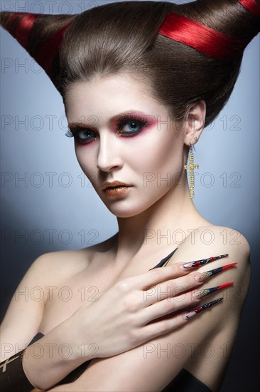 The girl in an image of the demon-tempter with long nails and haircut in the form of horns. Picture taken in the studio on a gray background