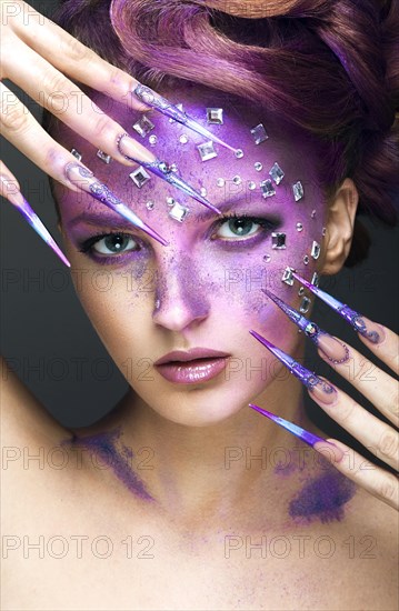 Girl with bright purple creative makeup with crystals and long nails. Beauty face. Picture taken in the studio on a gray background